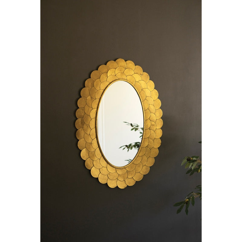 The Layered Gold Scallop Framed Mirror by Kalalou reflects plant leaves, adding chic decor to a dark wall.