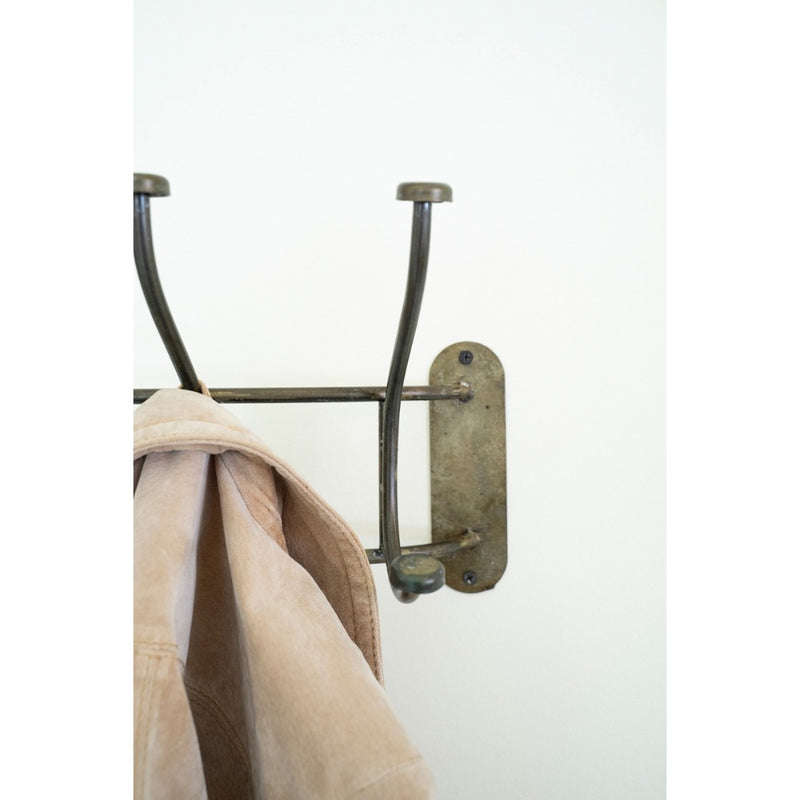 A beige jacket on a Kalalou Curved Iron Wall Coat Rack in a plain white entryway.