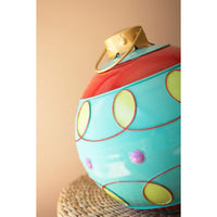 Close up view of a turquoise round ornament with yellow and purple polka dots orand gold trim