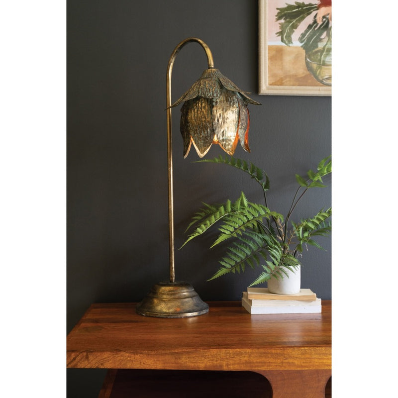 An Antique Brass Tulip Table Lamp by Kalalou adds elegance next to a potted fern on a wooden table.