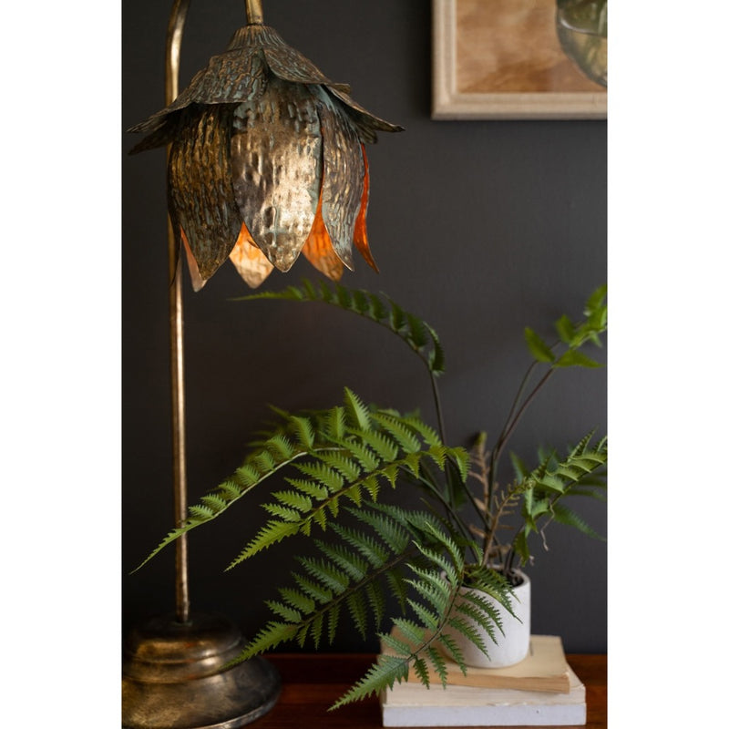 The Kalalou Antique Brass Tulip Table Lamp elegantly lights up beside a potted fern on a wooden table.
