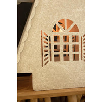 A close-up of a textured beige house with window cutout, glowing with warm light, mounted on a wooden surface.