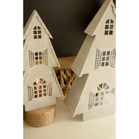 Two decorative miniature house-shaped ornaments in a light beige felt-like material, shown on a tabletop with a woven basket and a wooden stool against a dark background.