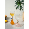 Two Kalalou pear base wine glasses, one with yellow liquid, sit on a table with a lemon and a plant.