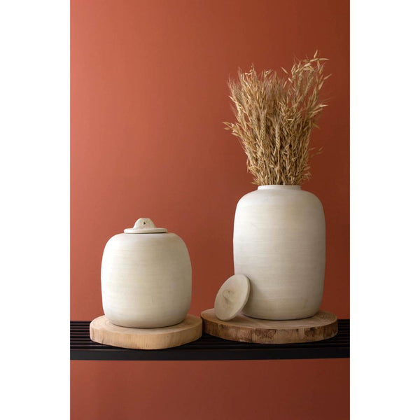 Two ceramic jars with wooden bases against a red-brown background