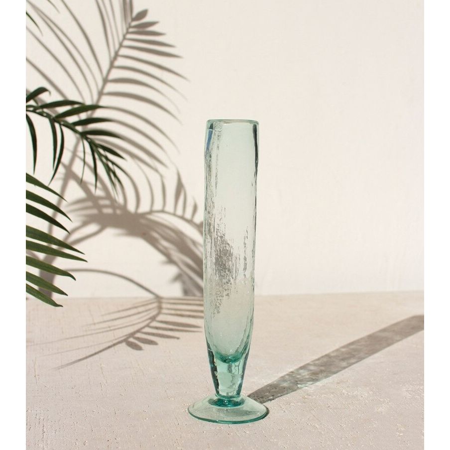 Tall turquoise glass vase on a light surface with palm leaf shadows