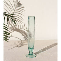 Tall turquoise glass vase on a light surface with palm leaf shadows