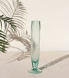 Tall turquoise glass vase on a light surface with palm leaf shadows