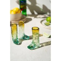 Three green glass boot-shaped shot glasses on a light surface with lemons and limes in the background.