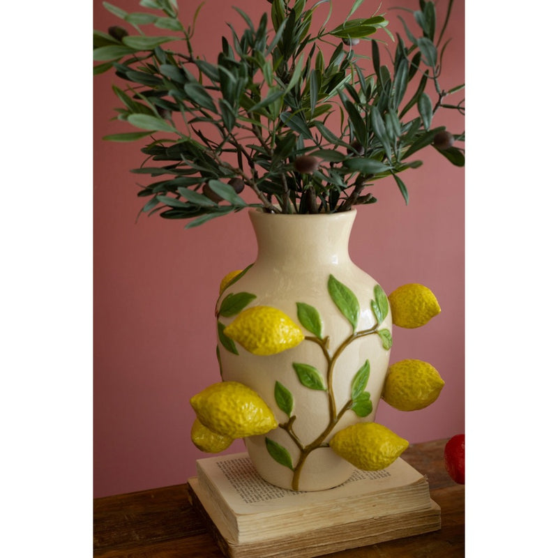 Kalalou's Ceramic Lemons Vase with leafy branches is a statement piece on a book against a pink wall.