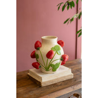 Ceramic vase with strawberry design on a wooden surface against a pink wall.