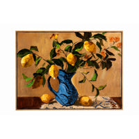 A framed still life painting featuring yellow lemons on branches with green leaves, arranged in a bright blue pitcher on a patterned cloth against a warm beige background.