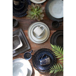 A wooden table featuring Kalalou's Glacier Ceramic Dinner Collection, cups, bowls, a succulent, and fern leaves.