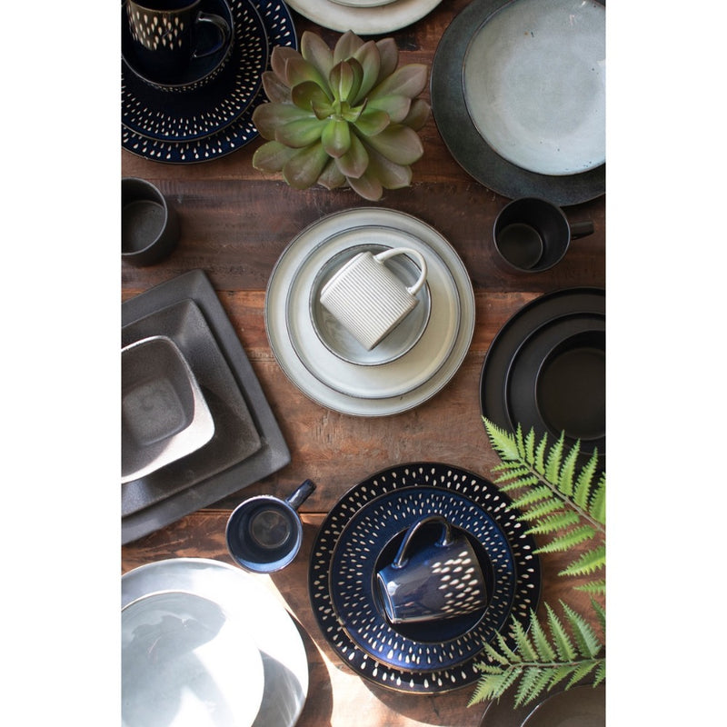 A wooden table featuring Kalalou's Glacier Ceramic Dinner Collection, cups, bowls, a succulent, and fern leaves.