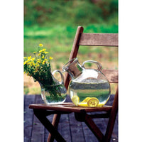 Clear glass pitcher with lemon slices and flowers on a wooden chair outdoors.