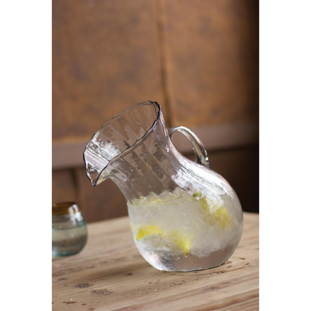 Clear glass pitcher with ice and lemon slices on a wooden surface