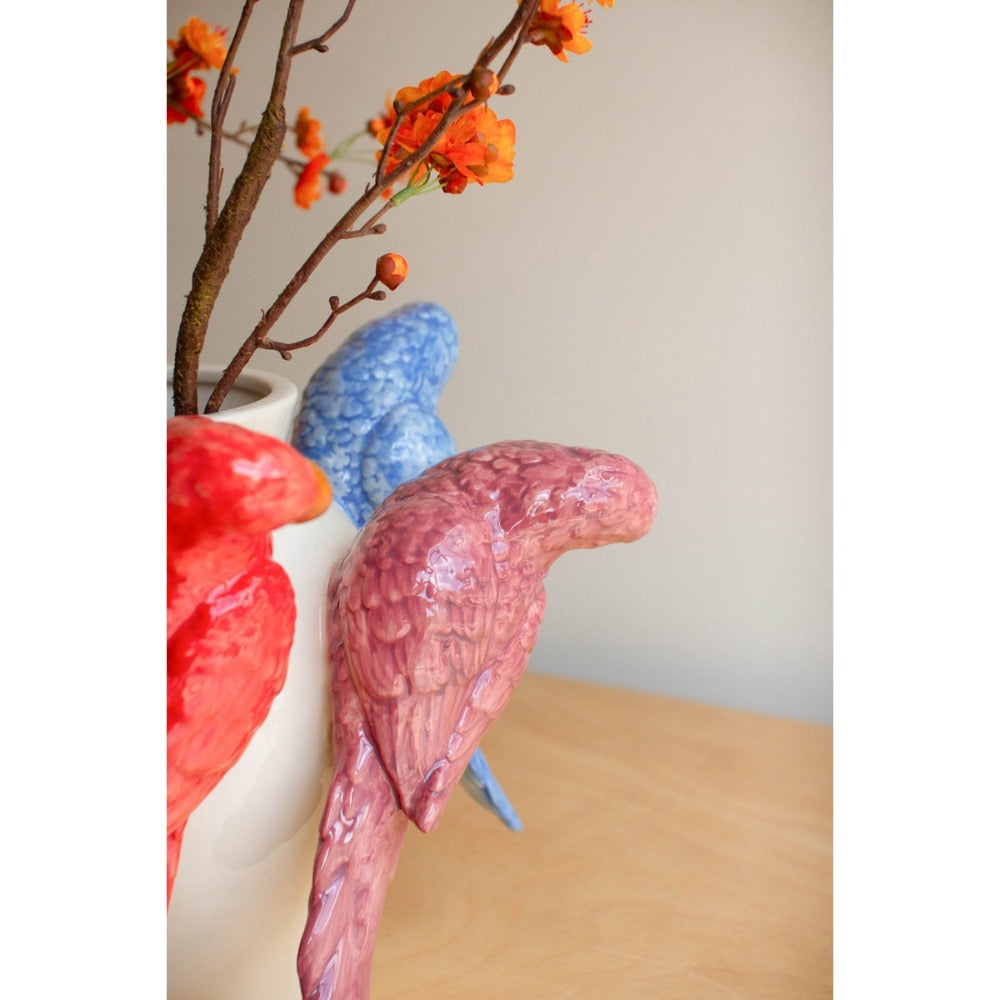 Colorful ceramic parrot sculpture with a vase and decorative branches on a wooden surface.