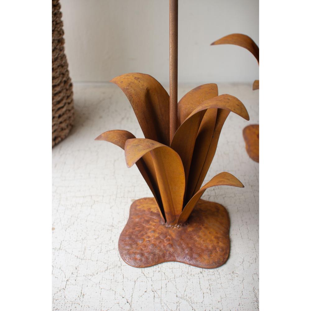 Rust-colored metal plant sculpture on a textured surface