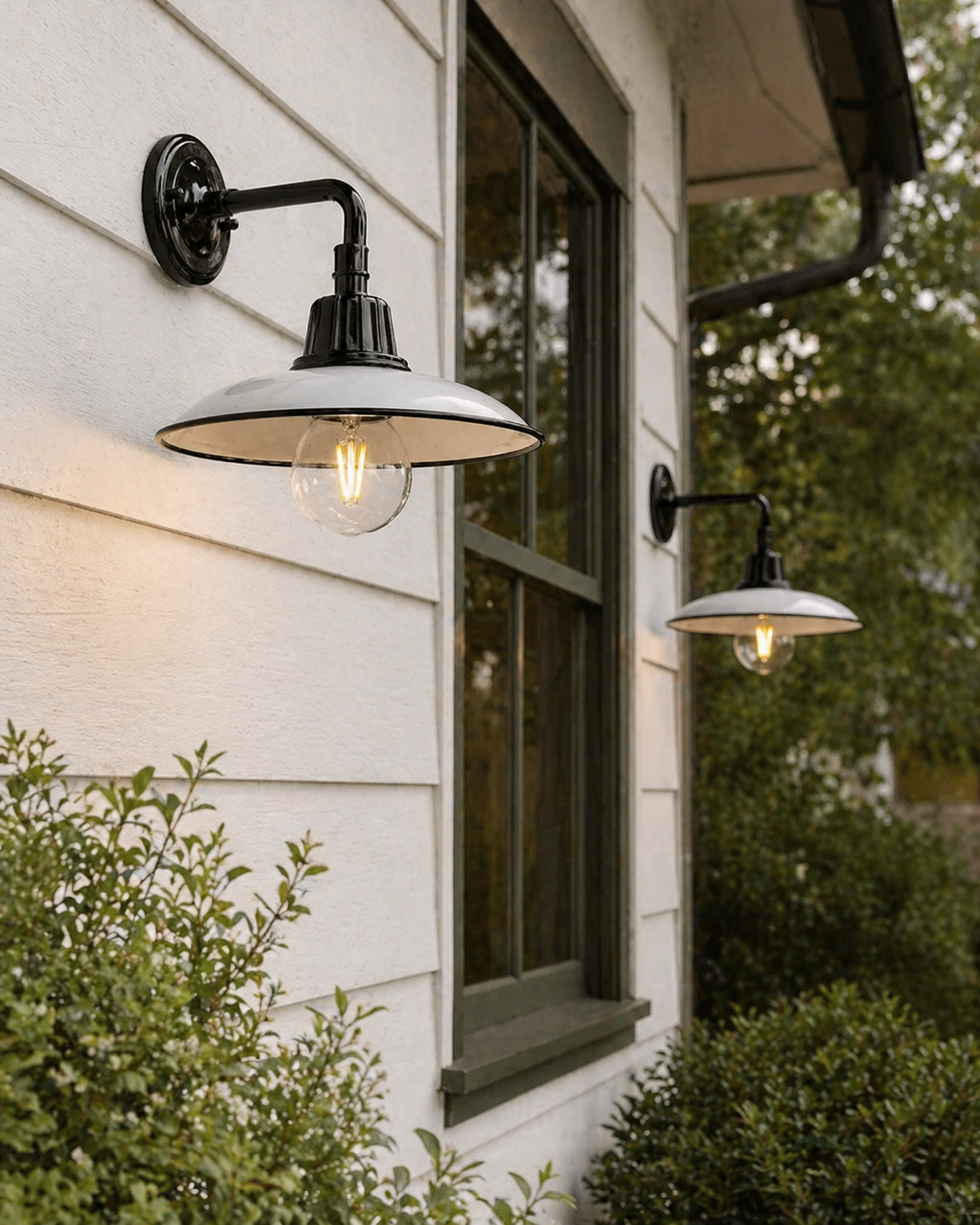 Outdoor wall lights on a house exterior with greenery around.