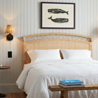 Cozy coastal bedroom with Kenian Charleston Rattan King Headboard, white bedding, whale art, and bench with a blue book.