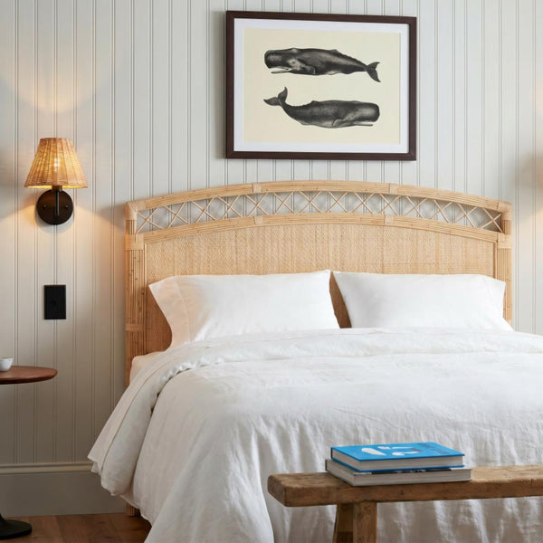 Cozy coastal bedroom with Kenian Charleston Rattan King Headboard, white bedding, whale art, and bench with a blue book.