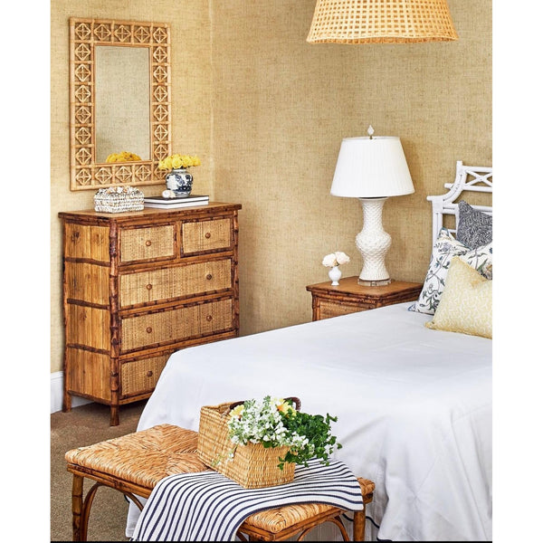 Cozy bedroom featuring Kenian Tortoise Shell Bamboo + Rattan Tall Drawer Chest, white bed, lamp, and floral basket.