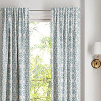 Chintz Mist Curtain Panels by Laura Park Designs frame a sunny window with green trees; a wall sconce is on the right.