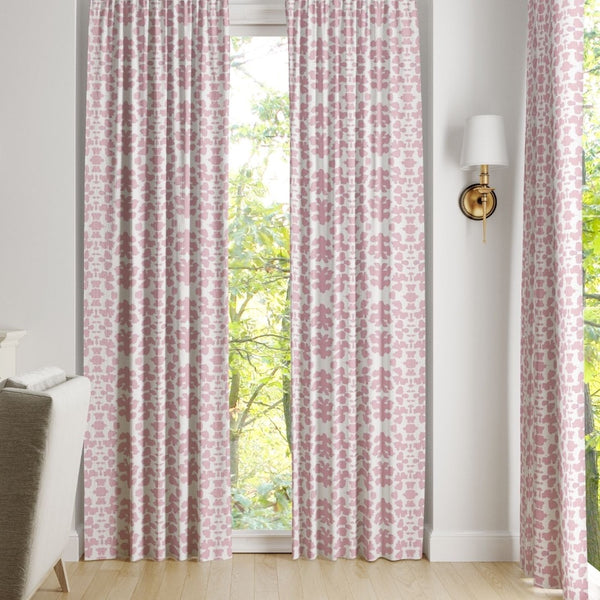 Chintz Rose Curtain Panels by Laura Park Designs, in pink and white, hang before a window with tree views.
