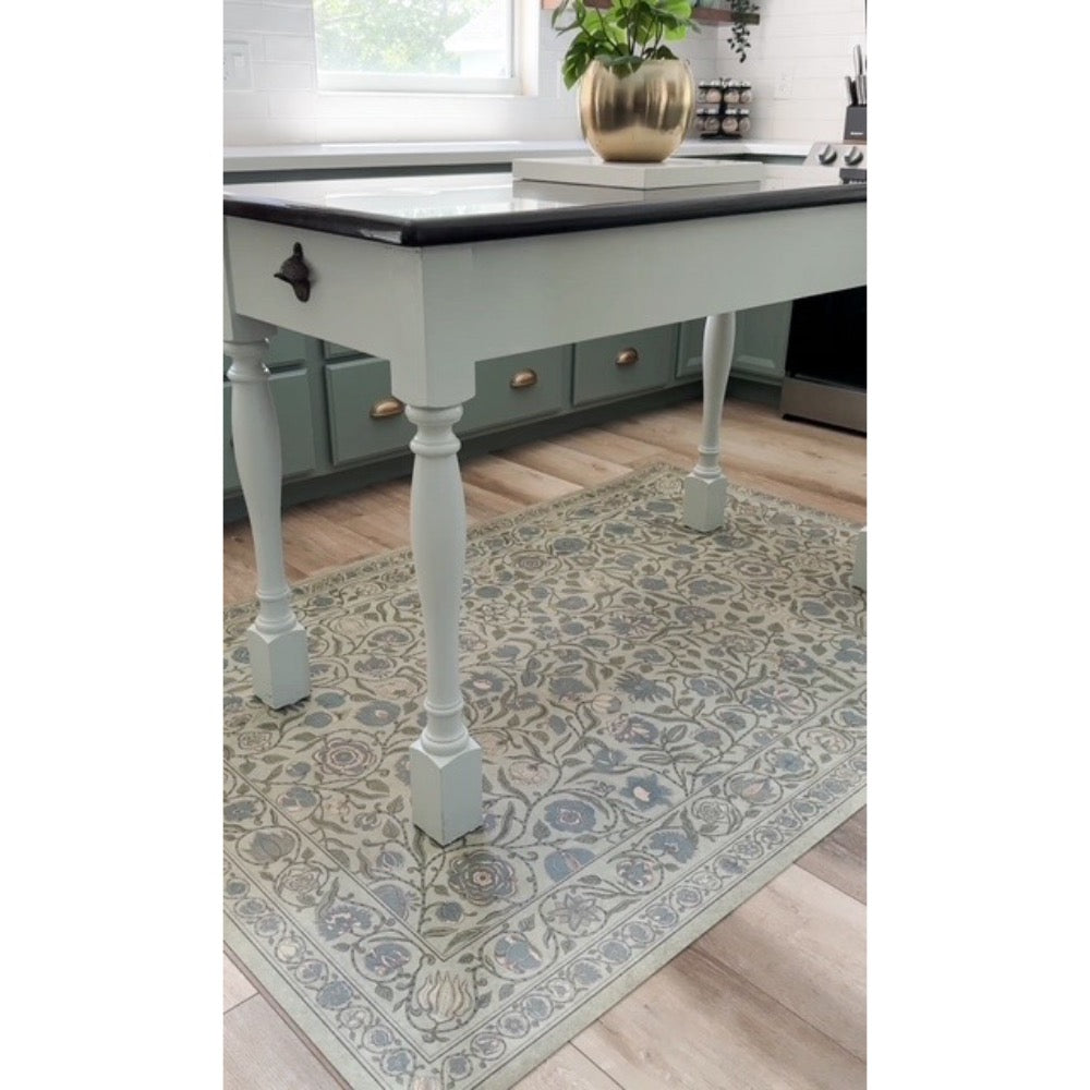 A Spicher and Company A Joy of Earth Vinyl Floor Mat lies under a light blue kitchen island with turned legs.