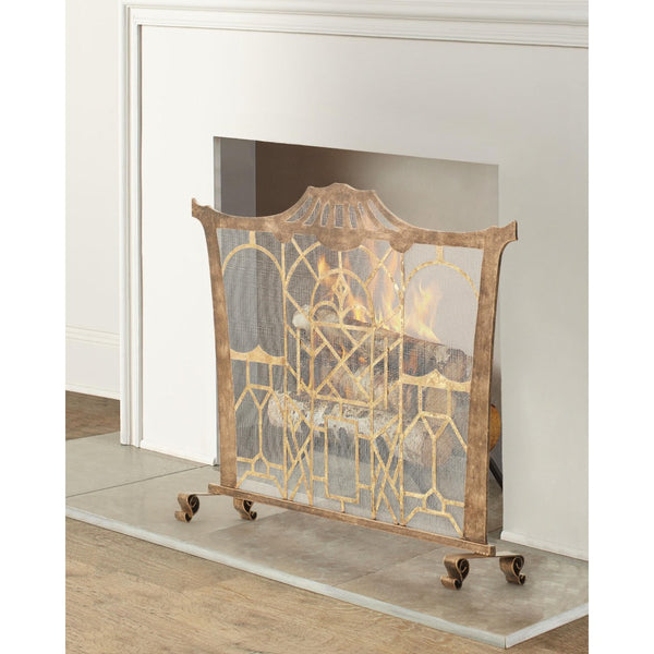 A decorative metal fireplace screen with an ornate gold geometric pattern over a weathered brown frame, shown standing on a hearth in front of a white fireplace.