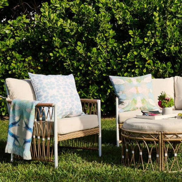 The Outdoor Chintz Mist Pillow by Laura Park Designs adds style to patio seating on grass with a lush green hedge backdrop.