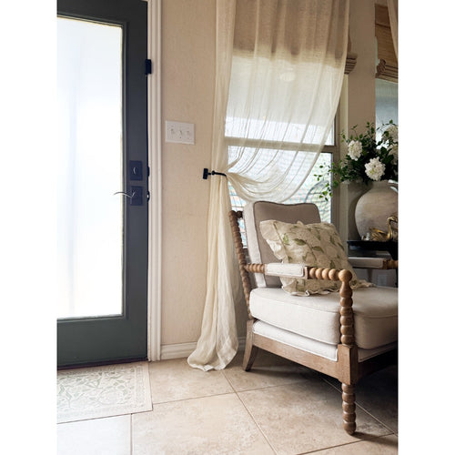 Beige armchair with floral pillow on Spicher and Company’s Antique Floral A Chilly Peace Vinyl Floor Mat by a window.