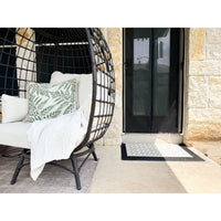 Round wicker chair with white cushions, leafy pillow, throw blanket, and Spicher and Company Clayton Vinyl Floorcloth.