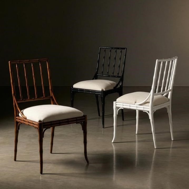 Three elegant dining chairs displayed in a studio setting: a dark brown wooden chair with a white cushion in the foreground, a black wooden chair with a white cushion in the center, and a white wooden chair with a white cushion on the right, against a dark brown background.