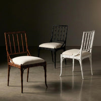 Three elegant dining chairs displayed in a studio setting: a dark brown wooden chair with a white cushion in the foreground, a black wooden chair with a white cushion in the center, and a white wooden chair with a white cushion on the right, against a dark brown background.