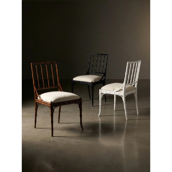Three elegant dining chairs displayed in a studio setting: a dark brown wooden chair with a white cushion in the foreground, a black wooden chair with a white cushion in the center, and a white wooden chair with a white cushion on the right, against a dark brown background.