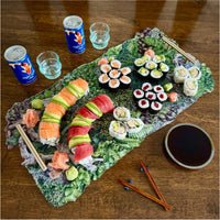 Assorted sushi on a decorative platter with drinks and soy sauce on a wooden table.
