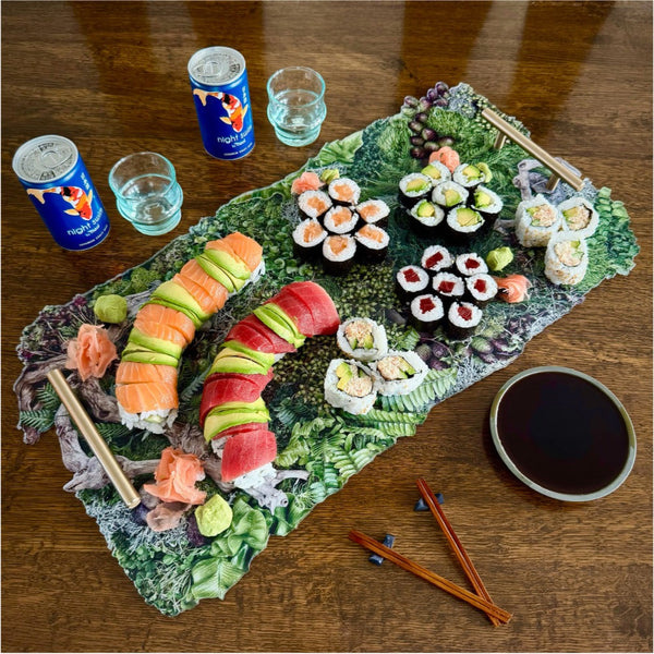 Assorted sushi on a decorative platter with drinks and soy sauce on a wooden table.