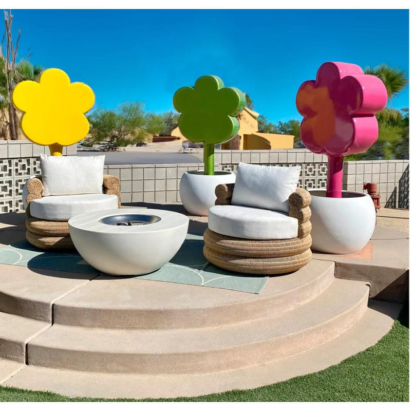 A patio setup featuring two round chairs, a fire pit table, and stylish flower-shaped decorations is beautifully complemented by adding a touch of artistry with the Indoor/Outdoor Flower Power Fiberglass Sculpture from Gold Leaf Design Group to elevate the ambiance.