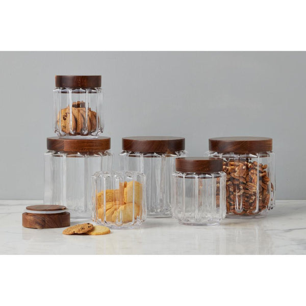 Set of glass jars with wooden lids on a white surface against a gray background
