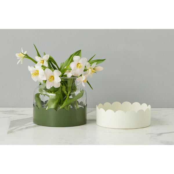 Glass vase with white flowers and green leaves on a white surface with a gray background