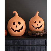 The Kalalou Terracotta Jack-O-Lanterns (set of 2) feature smiling faces on a dark wood surface against a gray wall.