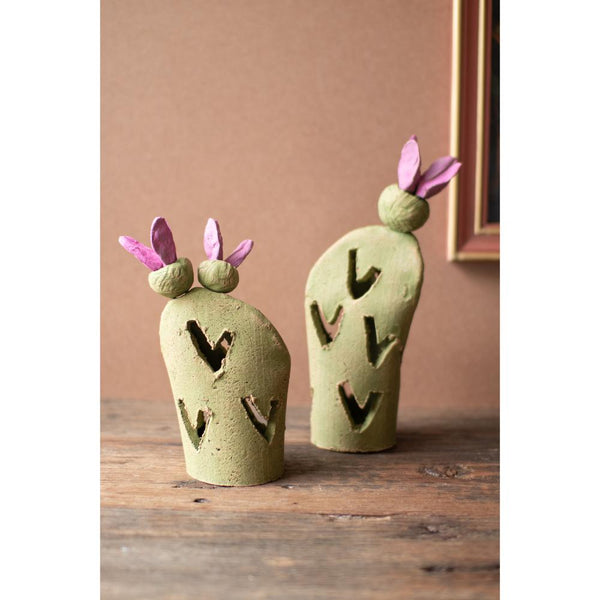 Two green ceramic cactus-shaped objects with pink bunny ears on a wooden surface.