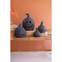 Two small black clay jack-o-lanterns by Kalalou sit on a wooden table with books, set against an orange wall.