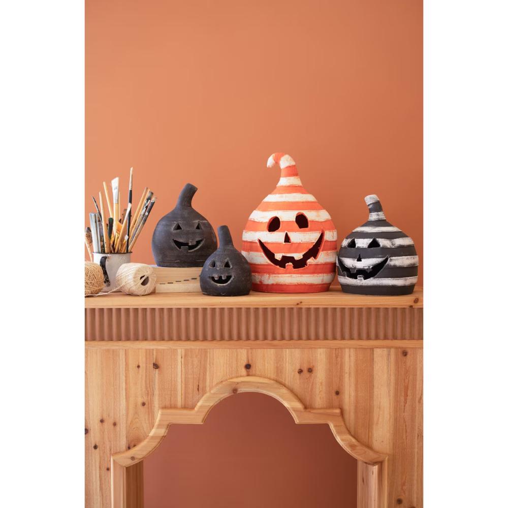 Two striped, handcrafted Kalalou Small Black Clay Jack-O-Lanterns on a mantel with paintbrushes against an orange wall.