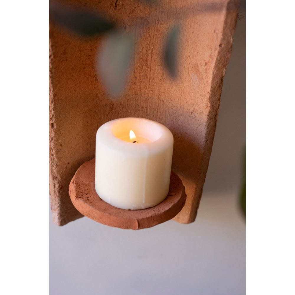 Candle in a clay holder against a textured wall