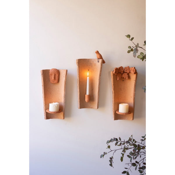 Three terracotta wall sconces with candles on a white wall.