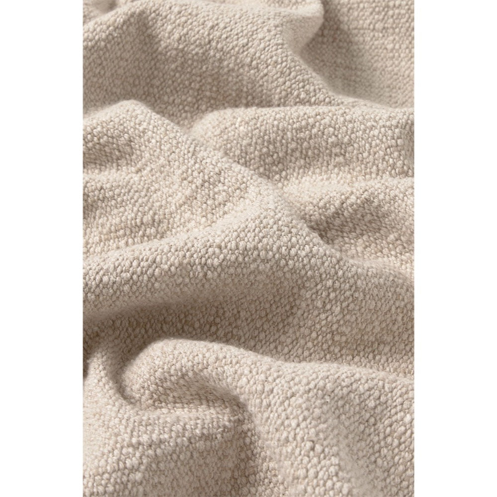 A close-up of a soft, textured beige fabric with a bouclé or chenille-like surface, shown in gentle folds and drapes.