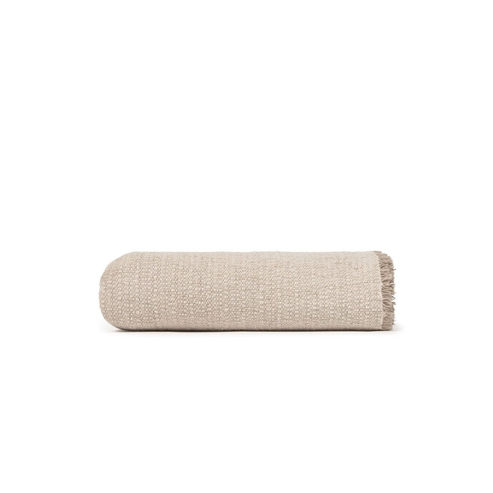 A folded beige woven throw blanket with fringed edges, shown on a plain white background.