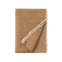A folded woven throw blanket in a warm tan-brown color with white fringed edges, shown on a solid white background.